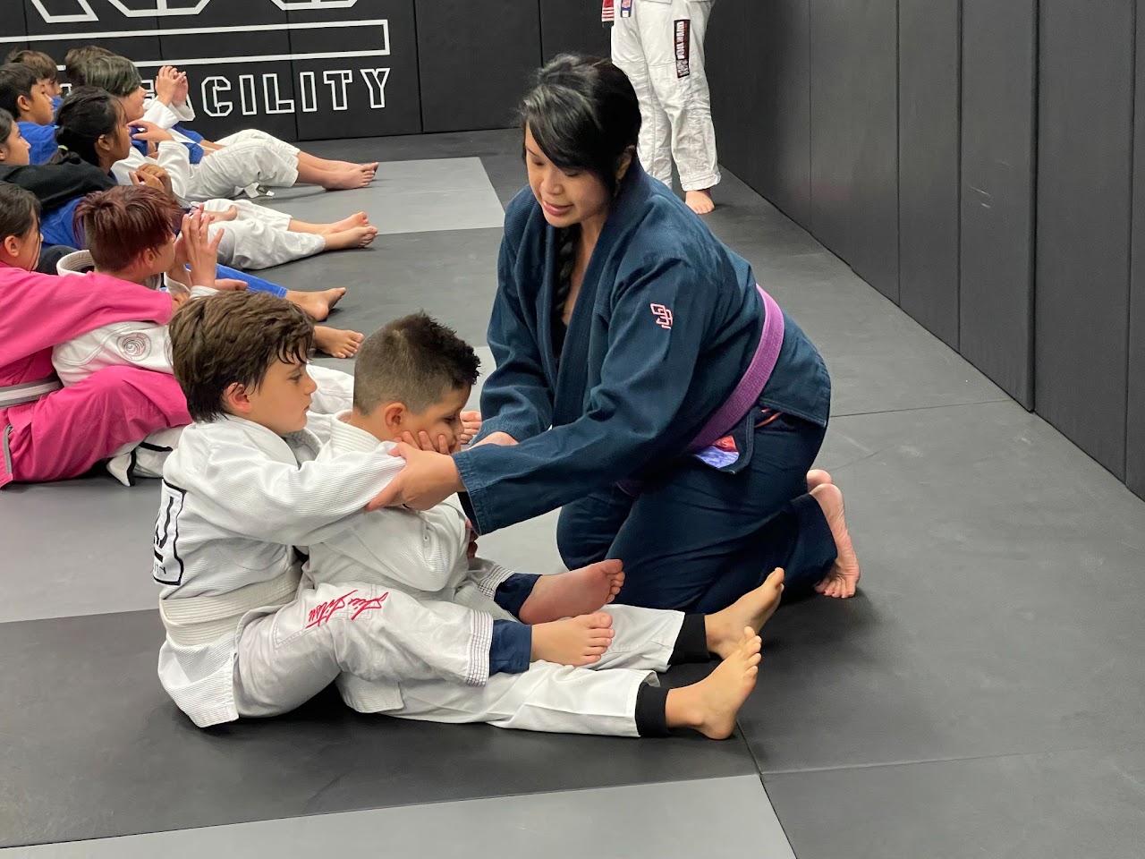 An instructor helping children learn jiu jitsu at TKJJ